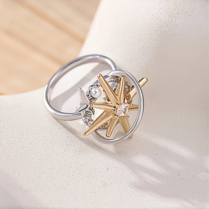 Two-tone starburst ring close-up, open silver band with a gold starburst charm featuring a clear crystal centre, small silver star and pearl accent