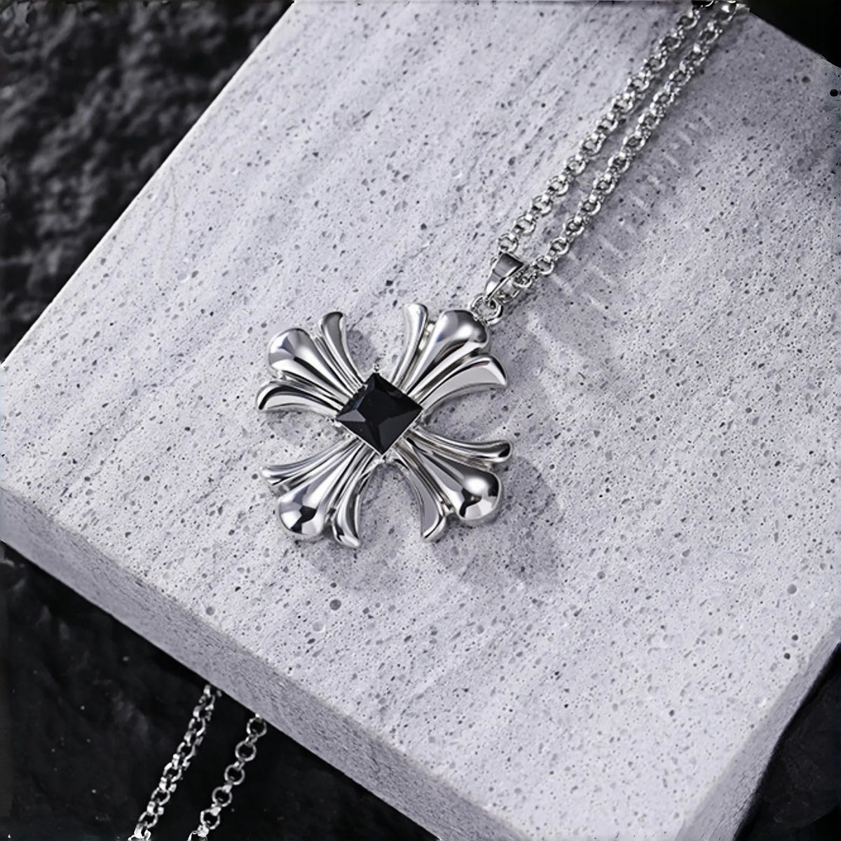 Gothic cross necklace close-up, silver cross pendant with black square stone on a grey stone surface