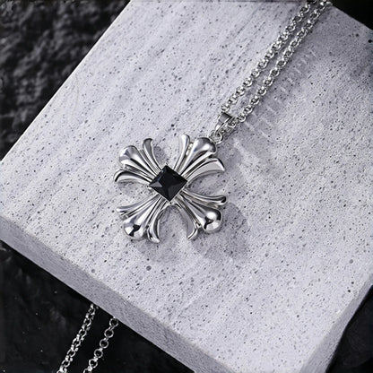 Gothic cross necklace close-up, silver cross pendant with black square stone on a grey stone surface