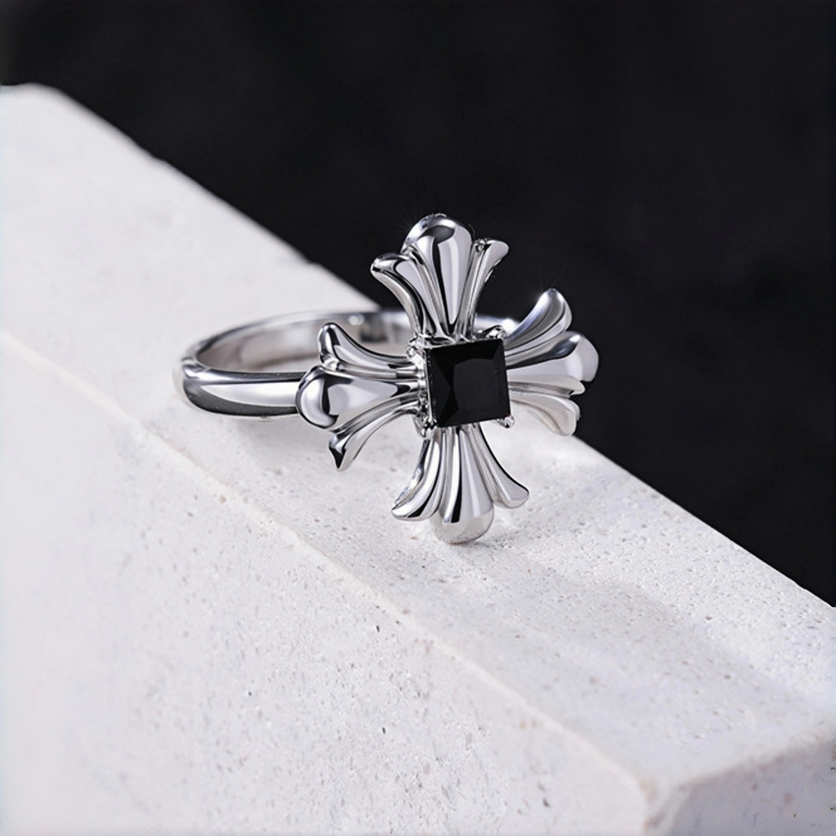 Gothic cross ring close-up, silver cross ring with black square stone on a white stone ledge