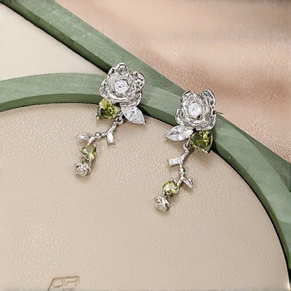 Vintage 3D rose stud earrings close-up, pair of silver rose studs with clear crystal centres, olive green crystal leaves and dangling crystal charms, worn on a model