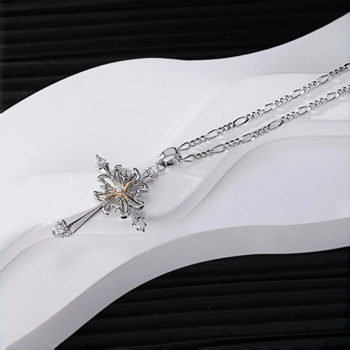 Vintage gothic cross pendant necklace close-up, silver cross with rose gold flower centre and clear crystal accents, on a figaro chain, resting on a white curved display