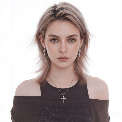 Front view of a model wearing an ornate cross pendant necklace and mismatched silver-tone cross drop earrings.
