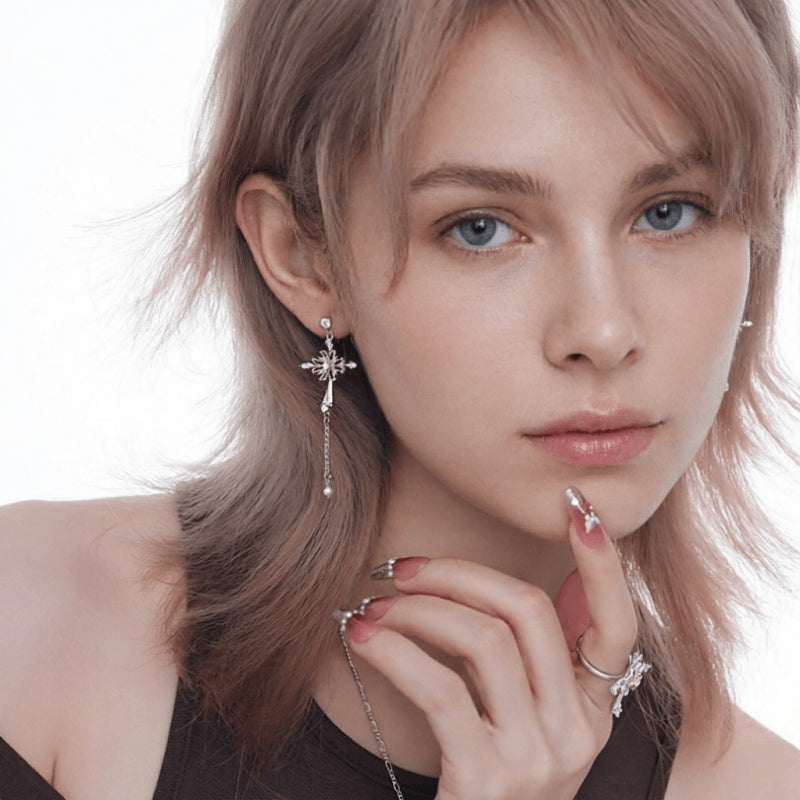 Model wearing an ornate silver-tone cross earring with a gold-tone centre and long dangling chain.