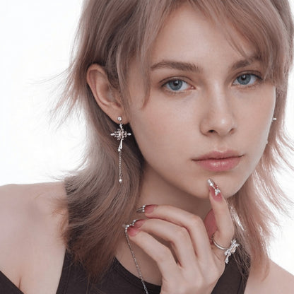Model wearing an ornate silver-tone cross earring with a gold-tone centre and long dangling chain.