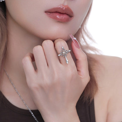 Close-up of a model wearing an ornate silver-tone cross ring with a gold-tone centre and long pointed drop.