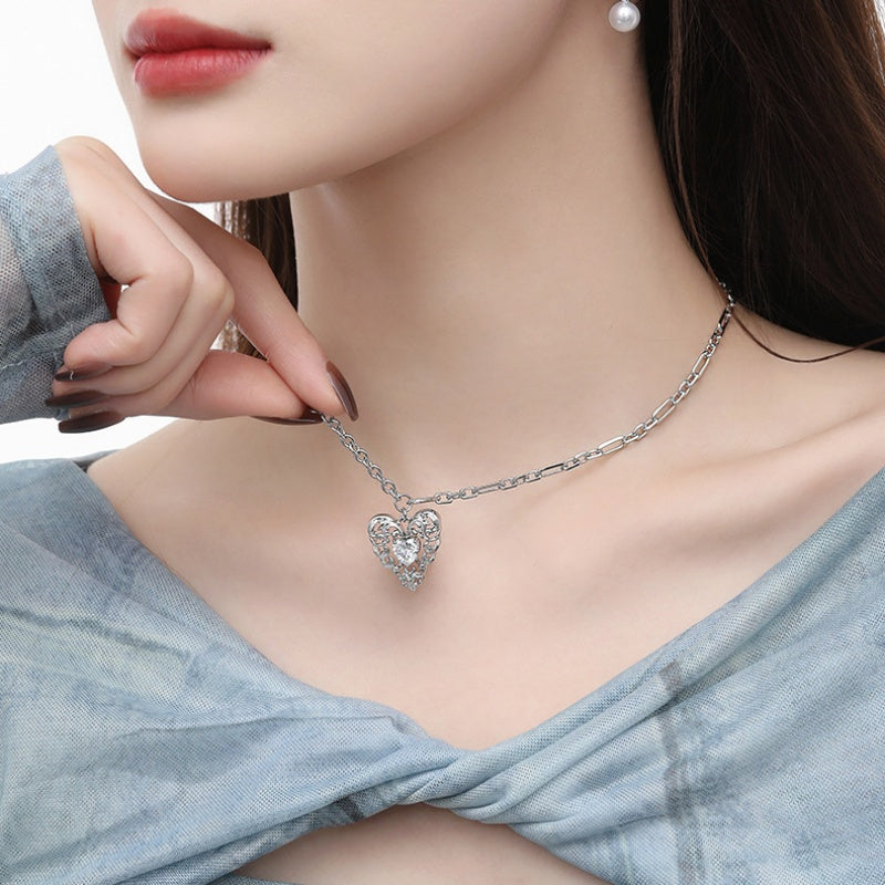 Model wearing a silver-tone ornate heart pendant necklace with a clear central stone on an asymmetric chain.