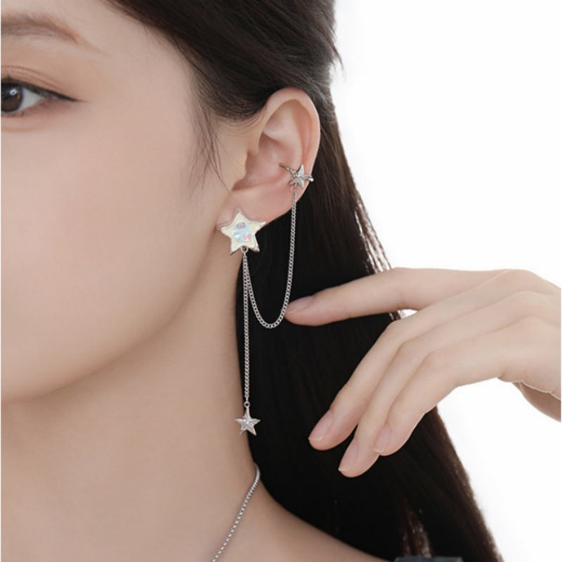 Close-up of a white star earring linked by a silver-tone chain to an upper ear cuff, with a dangling small star.