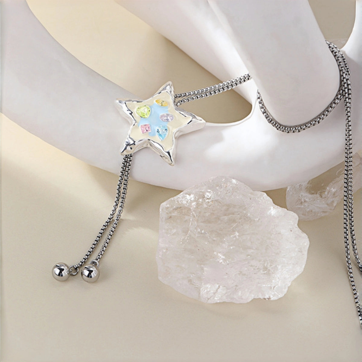Colourful star necklace close-up, silver enamel star pendant with pastel crystals on a box chain, draped over a display stand with a crystal rock in the background