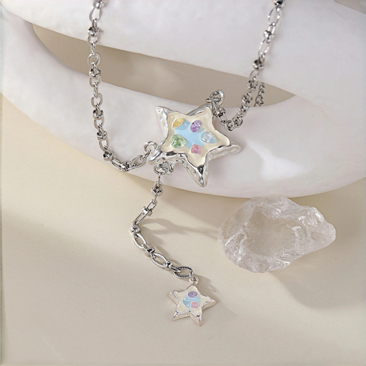 Enamel star lariat necklace close-up, silver enamel star pendant with pastel crystals on a rolo chain with a smaller star charm dangling below, beside a crystal rock