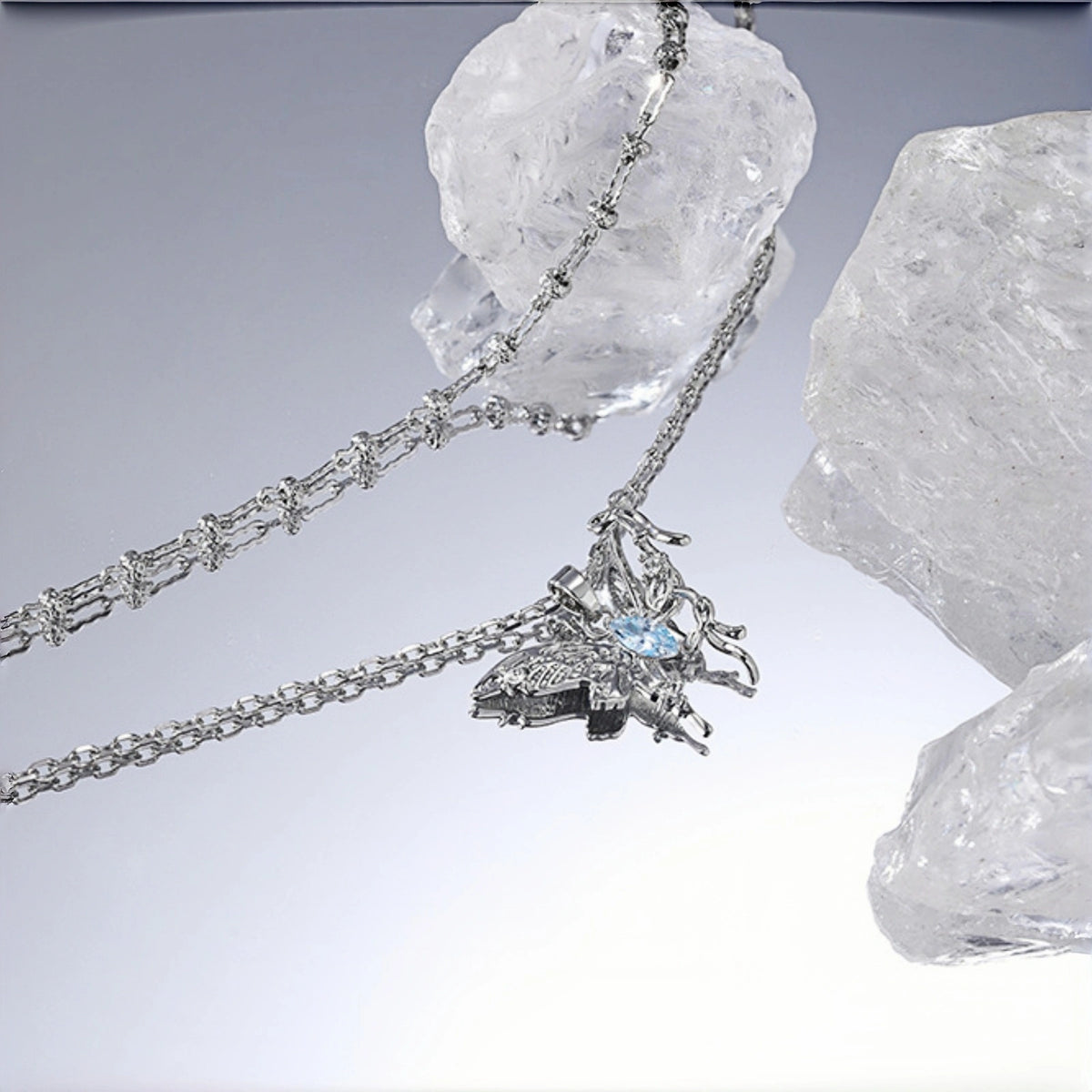 Fairy butterfly pendant necklace close-up, silver filigree butterfly pendant with a marquise blue crystal centre, on layered chains against crystal rocks