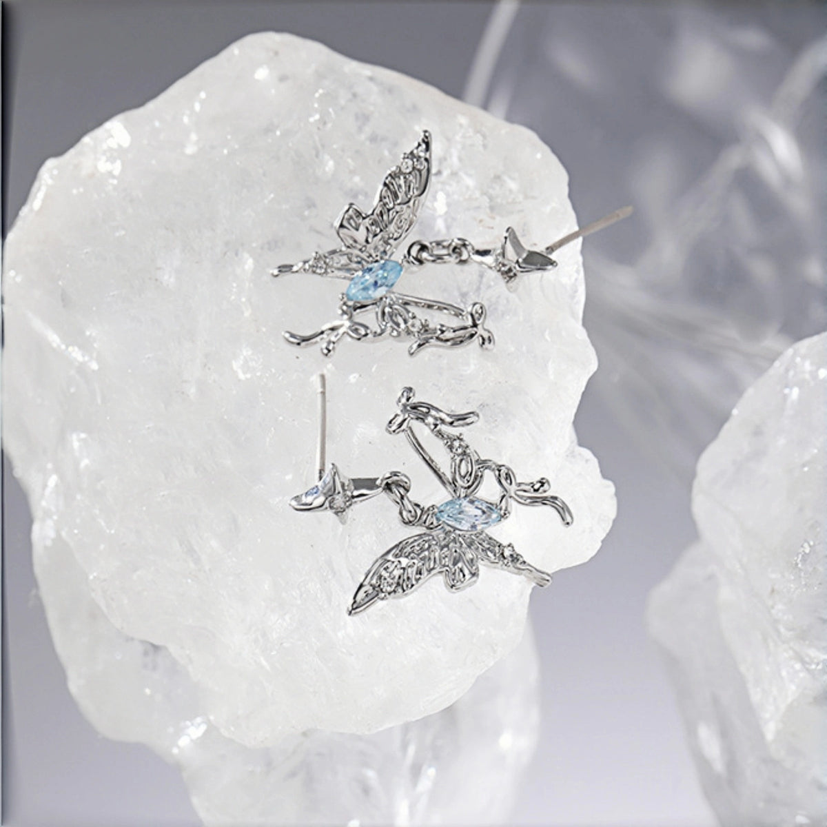 Fairy butterfly stud earrings close-up, pair of silver filigree butterfly studs with marquise blue crystal centres, resting on a crystal rock