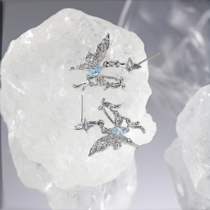 Fairy butterfly stud earrings close-up, pair of silver filigree butterfly studs with marquise blue crystal centres, resting on a crystal rock