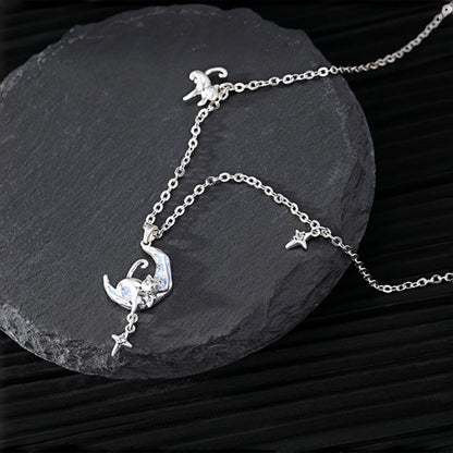 Moon and cat necklace close-up, silver crescent moon pendant with a curled cat charm and dangling star, on a slate surface