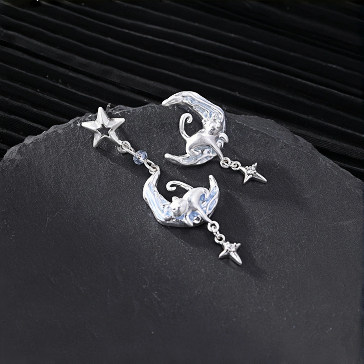 Moon and cat earrings close-up, pair of silver crescent moon drop earrings with cat charms, star studs and star drops