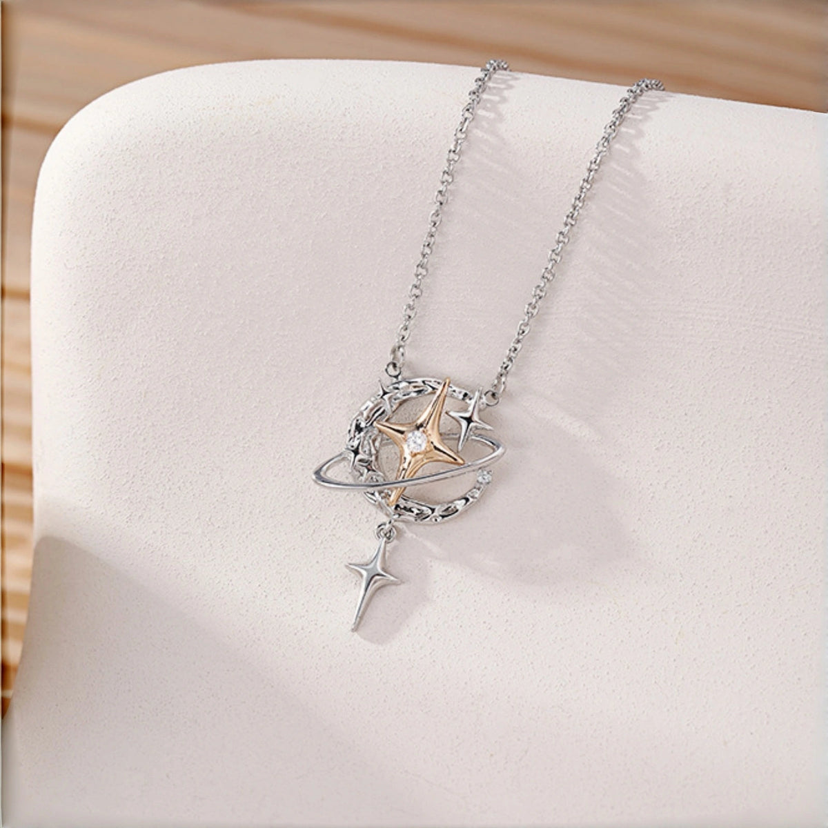 Y2K planet and star necklace close-up, silver orbit ring with gold star charm and dangling star pendant on cream fabric