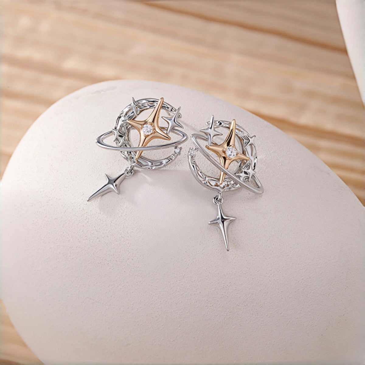 Y2K planet and star earrings close-up, pair of silver orbit hoop earrings with gold star charms and dangling star drops