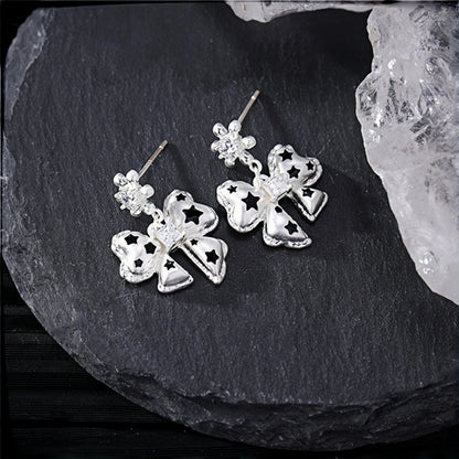 Silver bow drop earrings close-up, pair of bow charms with black star cutouts and small crystal stud tops, on a slate surface beside crystal rocks