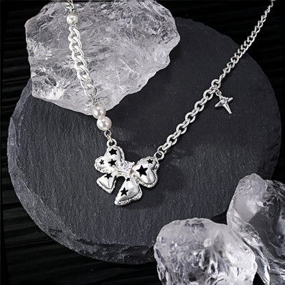 Silver bow pendant necklace close-up, bow charm with black star cutouts on a curb chain with pearl beads and a dangling star charm, on a slate surface with crystal rocks